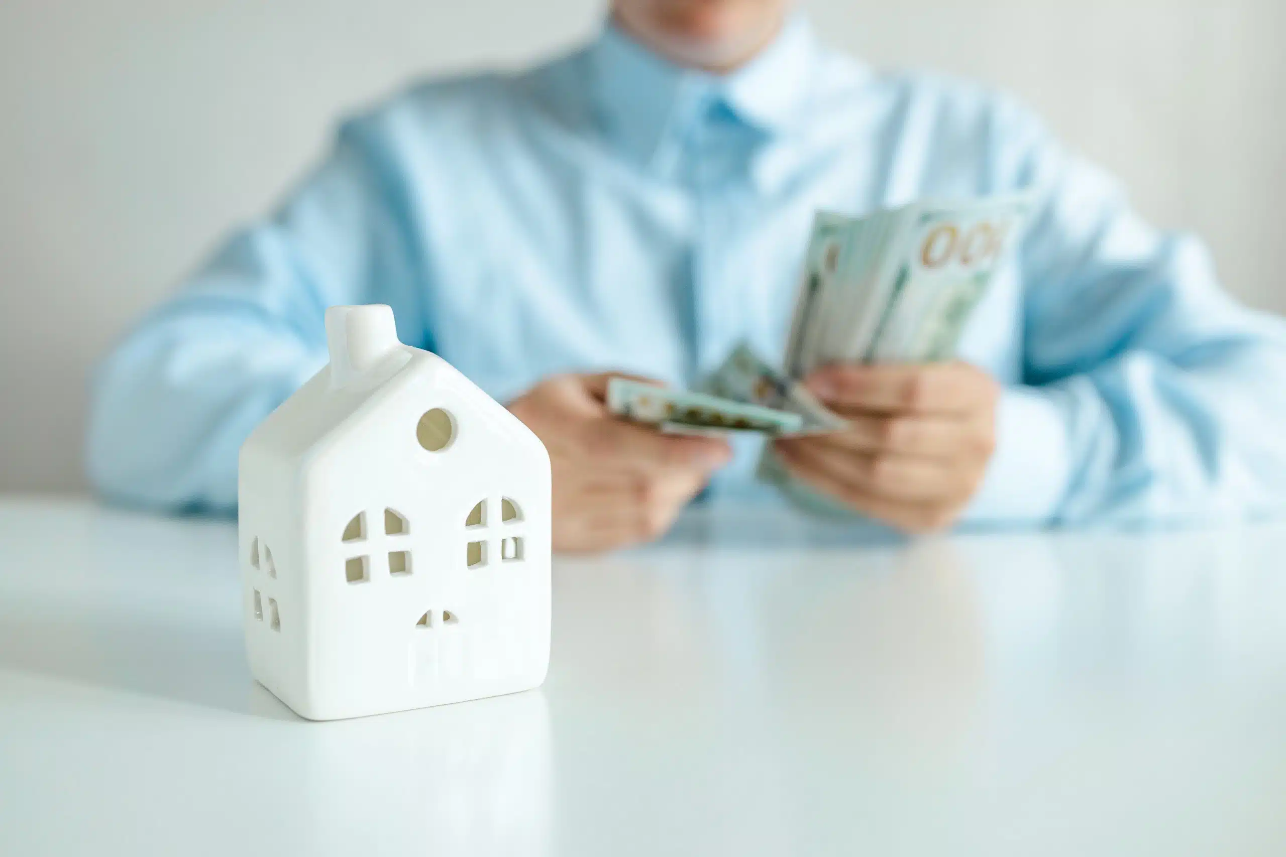 Businesswoman considers a bundle of dollar money. House model on a white table.