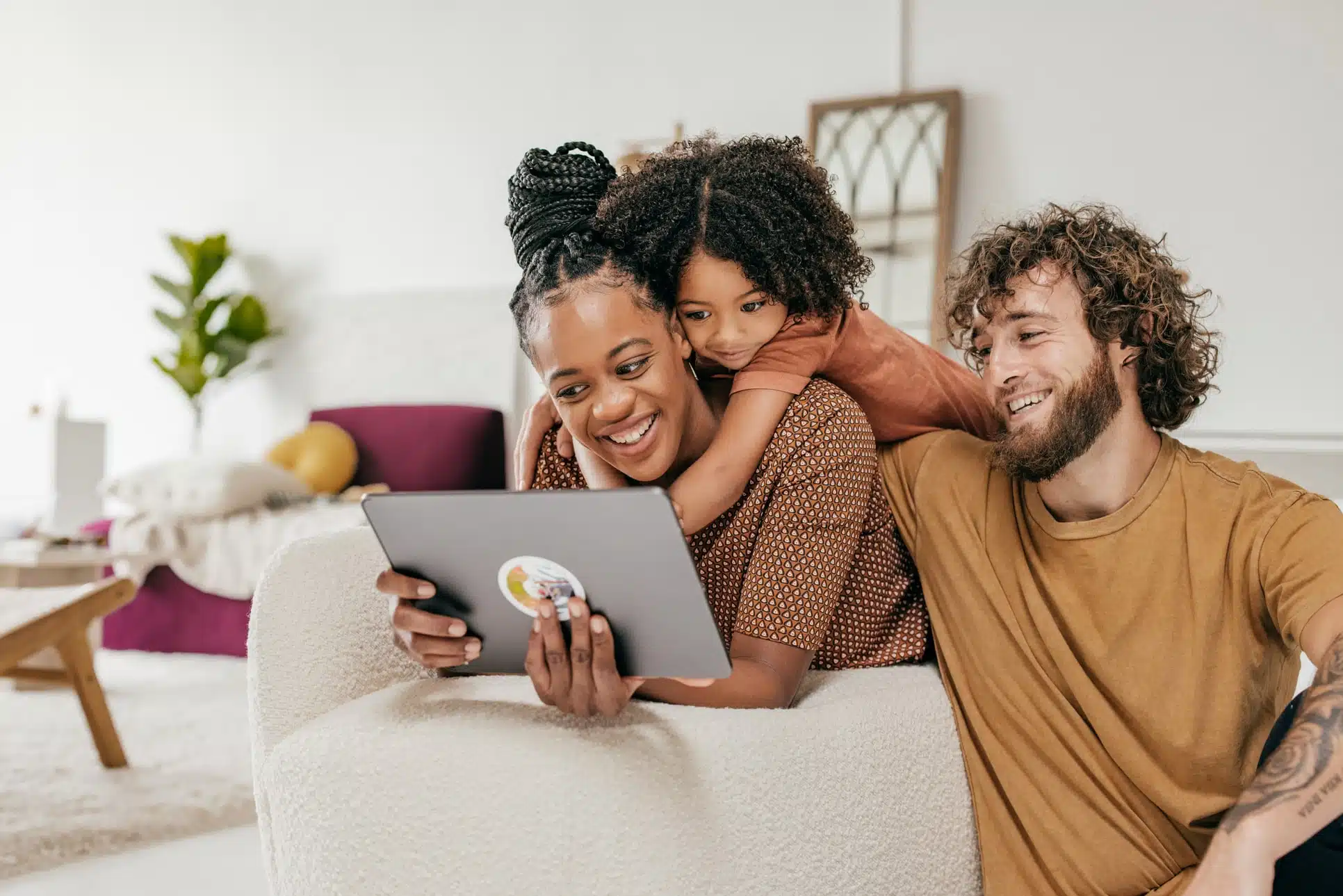 Famille dans un canapé qui regarde un écran de tablette en souriant