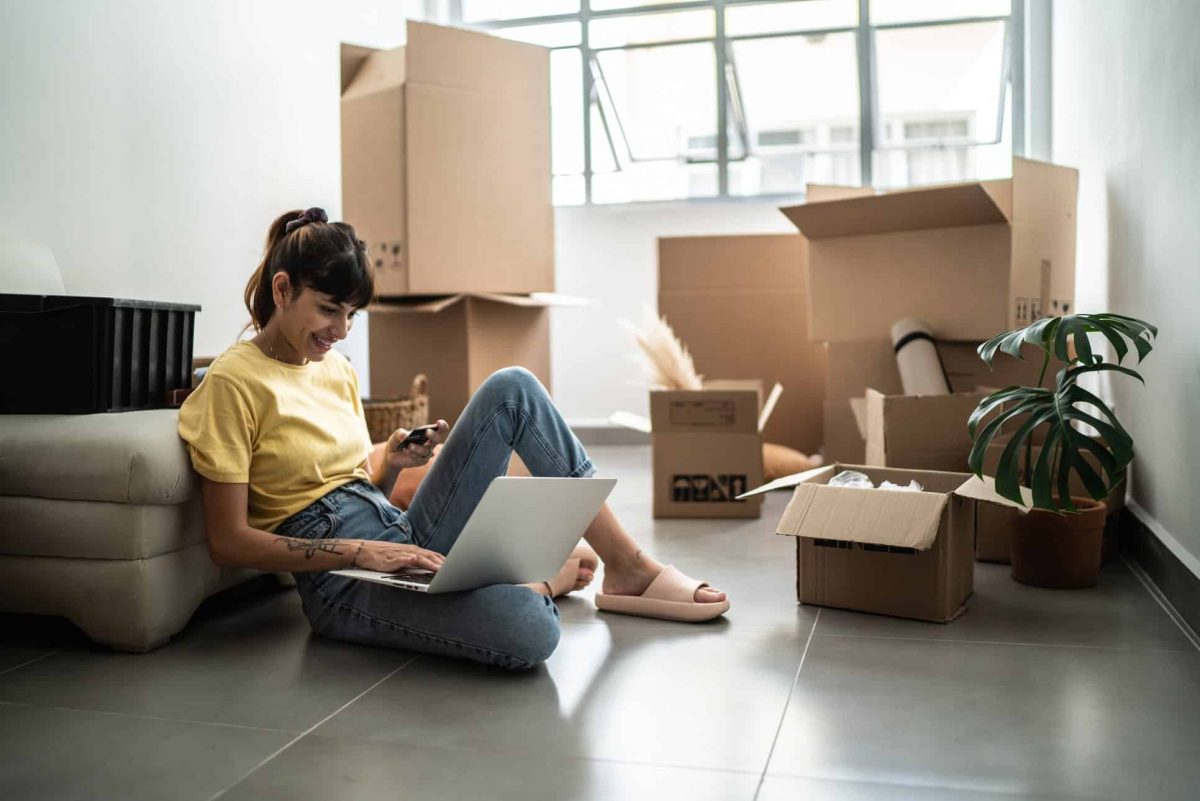 Jeune femme assise par terre dans son logement avec cartons de déménagement