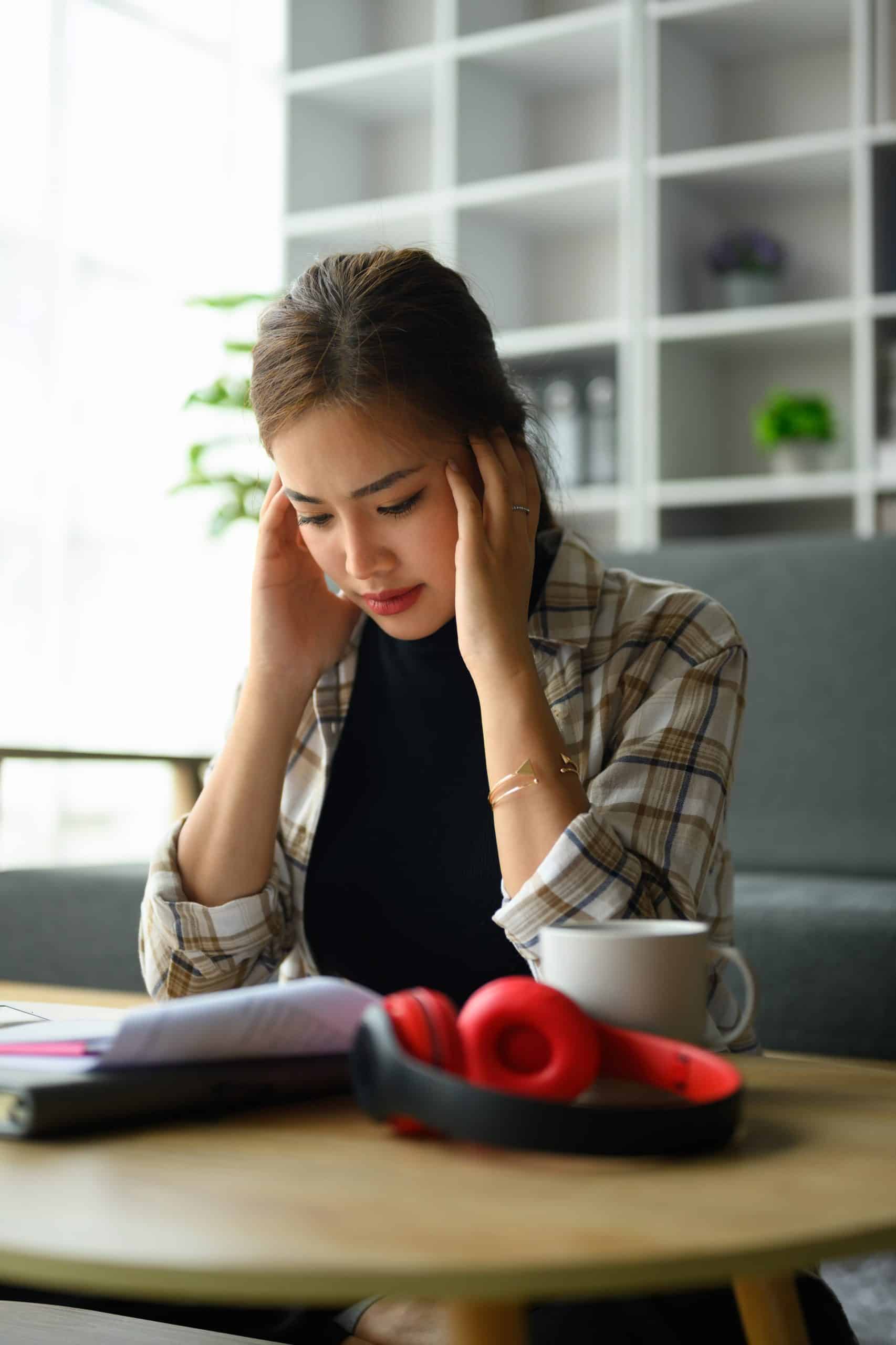 Stressed young woman holding head in hands, managing household finances frustrated with family financial problems.